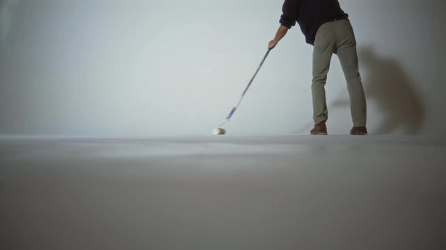 A worker paints a cyclorama in a photo studio with white paint