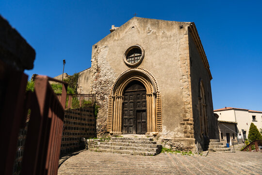 View of the historic Church of San Michele with its ancient stone facade and arched portal under a clear blue sky in Savoca, Sicily, Italy.