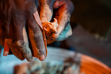 Obraz premium Close view of artisan hands shaping a tiny clay figurine in Zimbabwe, fingertips coated in ochre dust under warm directional light, with shallow depth of field.