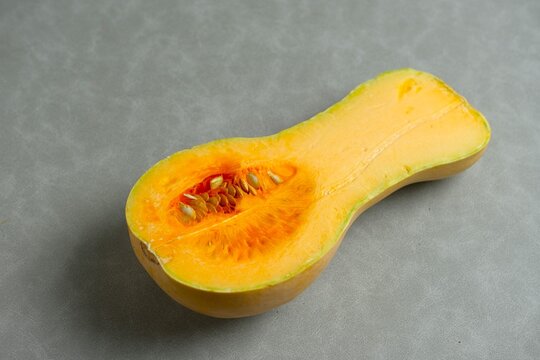 Halved butternut squash (Cucurbita moschata) showing orange flesh and seeds, also known as butternut pumpkin or labu madu, on a gray background.