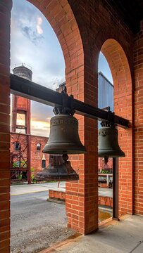 A photograph of two bronze bells hanging from a black metal rod, attached to a brick archway