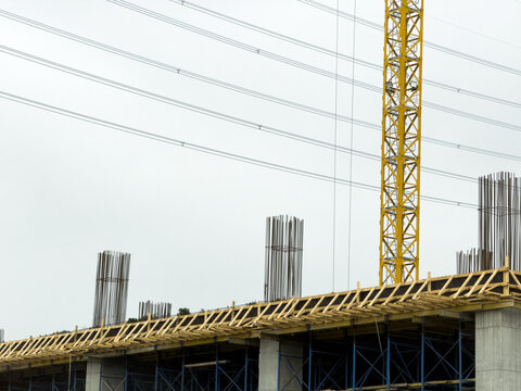 View of a construction site featuring a yellow tower crane, concrete pillars with steel rebar, and wooden formwork under an overcast sky in Beylikduzu, Istanbul, Turkiye.