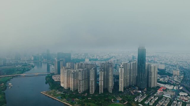 Aerial view of dense skyscrapers rising into heavy fog over riverside metropolis at dawn Ho chi minh city in Vietnam.