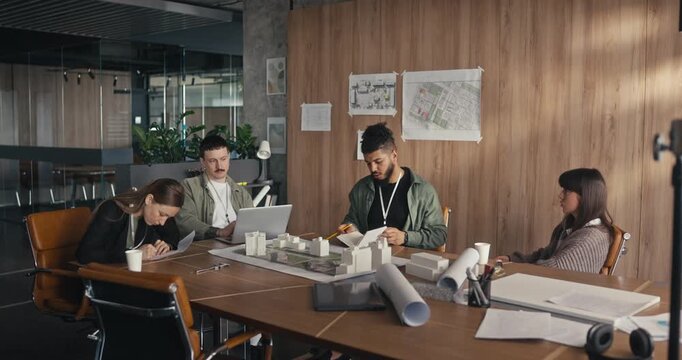 People gather around a table and discuss their project with papers and models present in an office setting