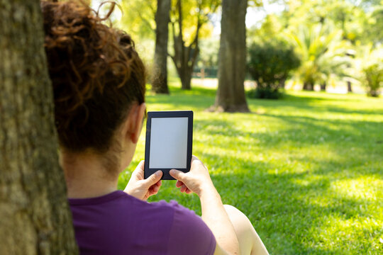 Caucasian woman reading ebook in park on sunny day