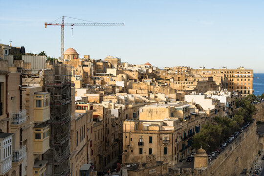 View of the historic limestone architecture and traditional balconies of the old town with a construction crane over the skyline in Valletta, Port Region, Malta.