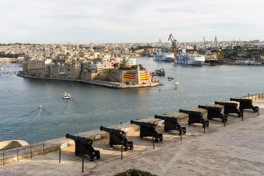 View of historic cannons at the Saluting Battery overlooking the Grand Harbour and the Senglea peninsula with industrial ships in the background Valletta, Port Region, Malta.