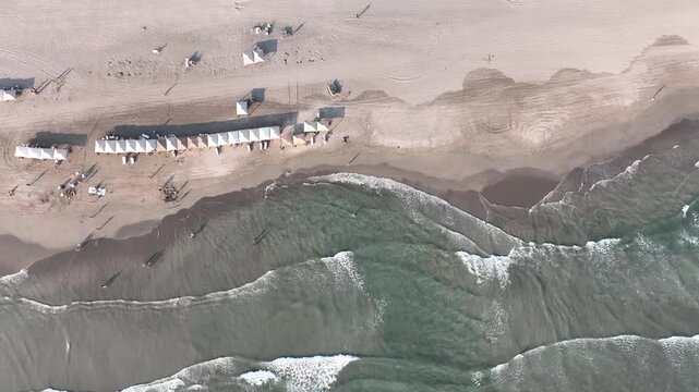Aerial view of ocean waves breaking on a sandy beach with umbrellas and tourists in Acapulco, Mexico