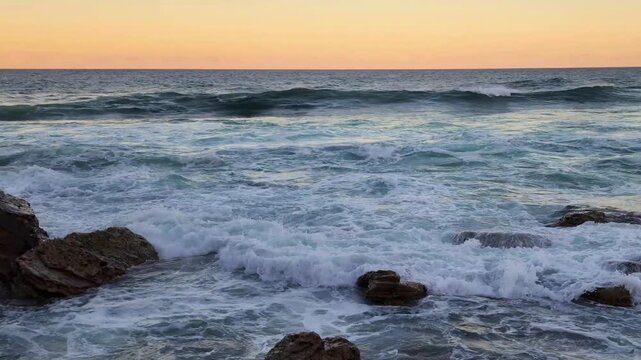 Sydney, Australia - Ocean waves crashing over shoreline rocks at sunset with warm horizon colours, capturing the natural beauty and tranquil seascape mood of the Northern Beaches coastline in motion. 