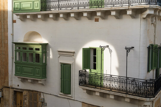 View of a traditional Maltese building facade with green wooden balconies and wrought iron railings under bright sunlight in Valletta, Port Region, Malta.