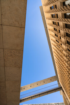 View of the modern limestone facade of the Parliament House with geometric patterns and a connecting bridge under a clear blue sky in Valletta, Port Region, Malta.