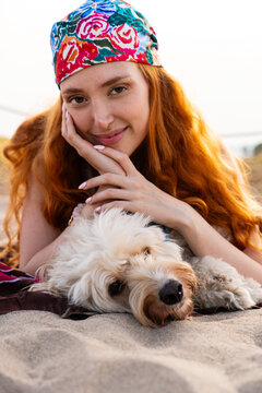 Red-haired woman relaxing with doodle dog on sand