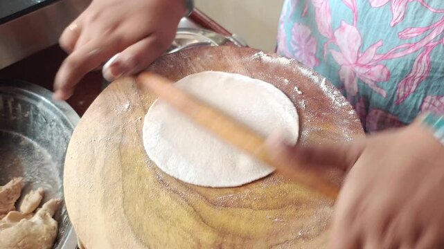 Close up of Indian woman rolling fresh dough with rolling pin to make round roti on a chakla