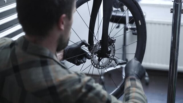 Professional bicycle mechanic adjusting a disc brake on a modern bike wheel in a repair workshop. Close-up of bicycle maintenance, cycling service and technical inspection.