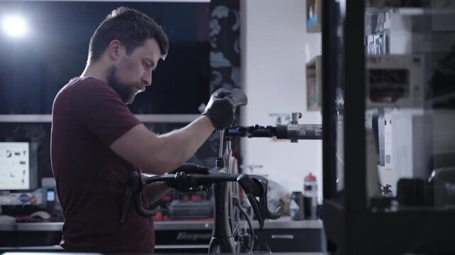 Male technician doing maintenance check on expensive black carbon fiber bike. Professional repair workshop, diagnostic equipment, high-utility technical service for premium cycling industry.