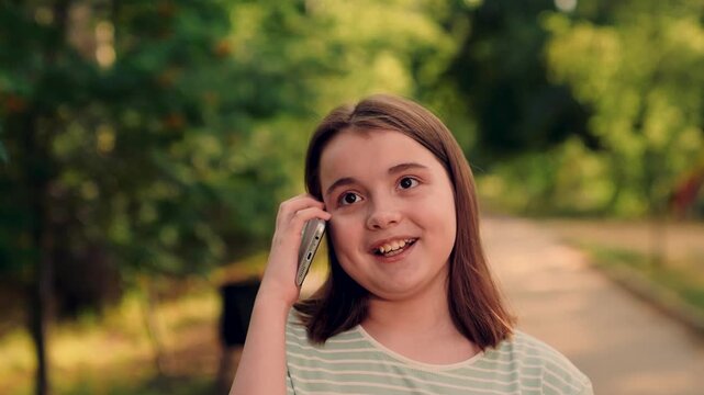 sweet girl smiling during phone conversation under shady park trees., listening carefully and laughing., natural bokeh and warm colors., girl enjoys phone call, nature background, smiling girl talking