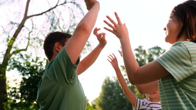 Happy children playing playground, children hands sun glare nature, boy girl friends playground, carefree childhood scene in a green park, lively group activity for children in the park, hands-up game