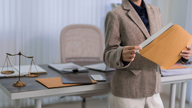 professional lawyer reviewing legal document folder standing in modern law office workspace with scales justice on desk business woman attorney preparing case
