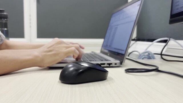 Close-up video of an employee hand operating a computer mouse while working on a laptop at an office desk, representing productivity, technology, and modern workplace activities.