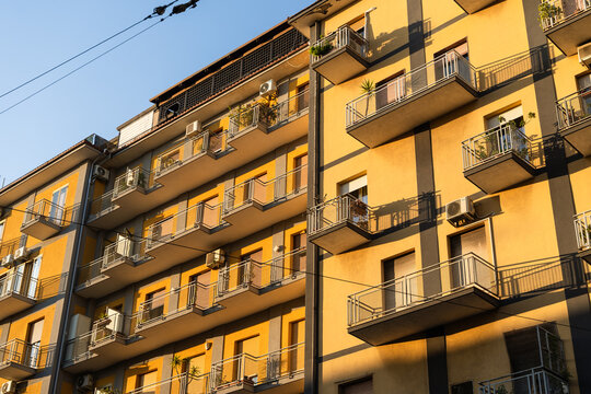 View of a yellow residential apartment building with numerous balconies and air conditioning units under a clear sky in Catania, Sicily, Italy.