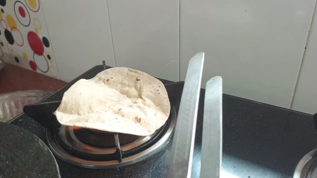 Cooking traditional Indian phulka roti on open gas flame using steel tongs