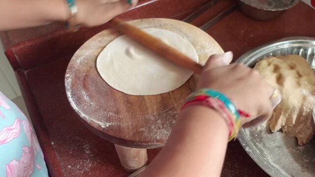 Side view of an Indian woman rolling wheat flour dough into a round roti on a wooden board