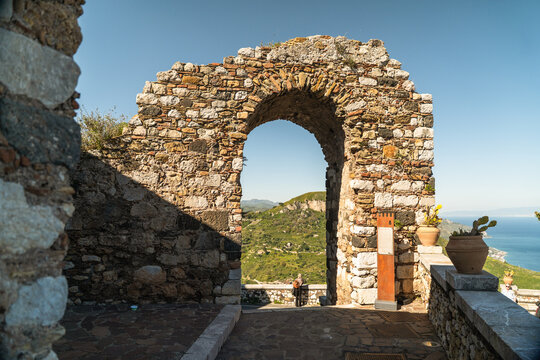View of an ancient stone archway overlooking green hills and the Mediterranean sea with terracotta pots in Castelmola, Sicily, Italy.