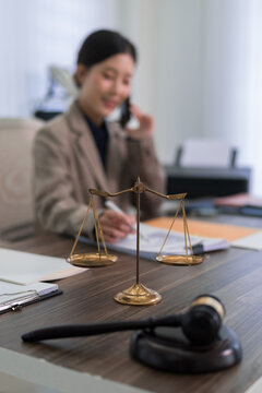 Asian female lawyer professional talking phone consulting client golden justice scale gavel law office desk modern business workplace legal advice professional