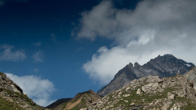 Majestic rocky mountain peaks under a dramatic blue sky with fast-moving white clouds, high alpine landscape in the Loetschental valley, Valais, Switzerland.