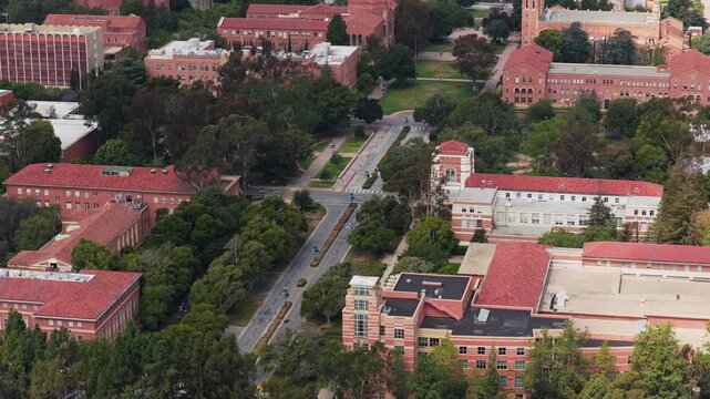 High angle establishing shot flying over University of California, Los Angeles campus buildings with traditional brick architecture and red tiled roofs in Southern California