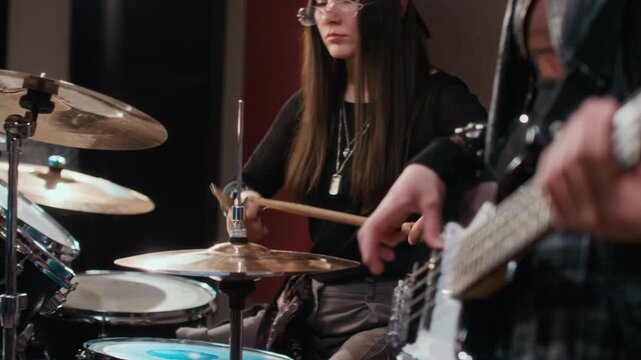 Caucasian female teenager playing drums while bandmate plays bass guitar during music rehearsal in studio. Footage is perfect for youth lifestyle or music education campaigns