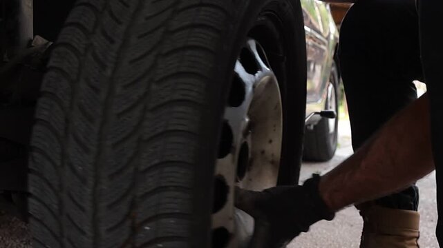 Mechanic removes a vehicle wheel and rolls it away after loosening the lug nuts. Close up automotive maintenance scene revealing the wheel hub and brake assembly.