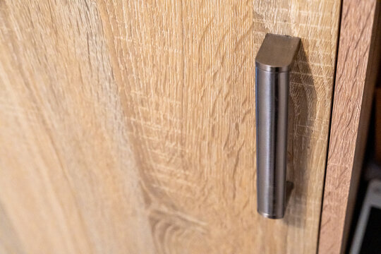 Close-up of modern cabinet wooden door with metal handle, showcasing contemporary furniture design and textures in a stylish interior setting