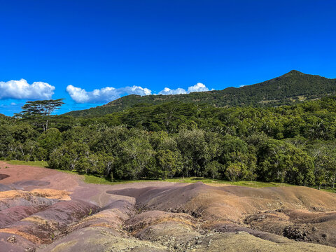 View of multi-colored sand dunes at Chamarel Seven Colored Earth Geopark with lush tropical forest and a mountain in Chamarel, Riviere Noire District, Mauritius.