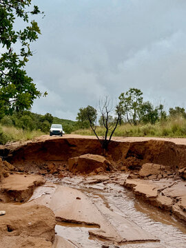 View of a white car stopped at a collapsed dirt road caused by soil erosion under an overcast sky in Thabo Mofutsanyana District Municipality, Free State, South Africa.