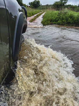 View of a 4x4 vehicle splashing through murky water on a flooded dirt road with lush green vegetation Thabo Mofutsanyana District Municipality, Free State, South Africa.