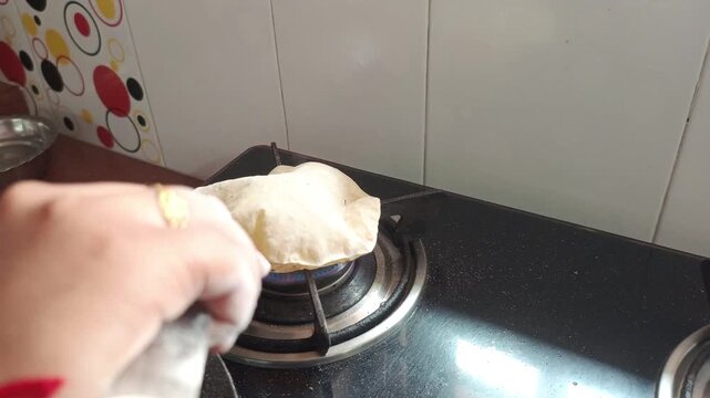 Making soft Indian phulka chapati by puffing it over an open gas stove flame