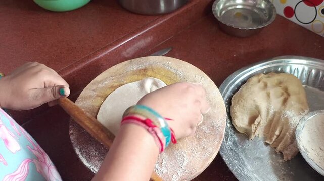 Top angle shot of an Indian woman rolling flatbread dough into a perfect round roti on a wooden board