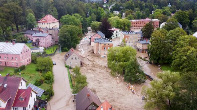A panoramic view of a river dangerously overflowing its banks and violently flooding homes and cars.