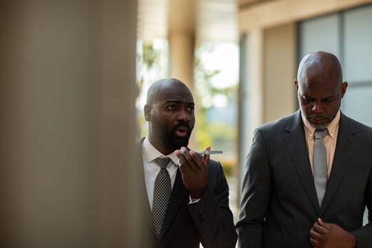 Two businessmen using smartphone voice message outside office building