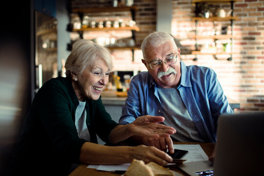 Happy senior couple using laptop in home kitchen