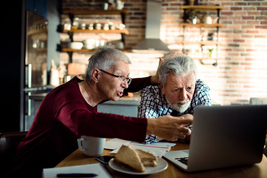 Senior couple managing finances on laptop in kitchen