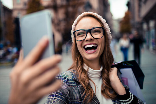 Smiling woman taking selfie with shopping bags on city street