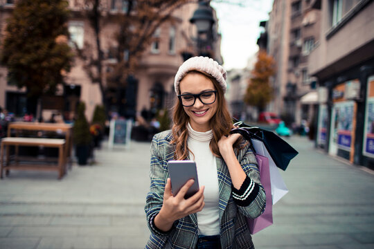 Smiling woman shopping with smartphone on city street