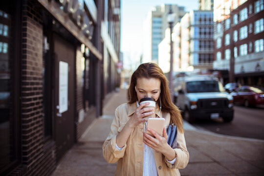 Young woman drinking coffee and using smartphone on city street