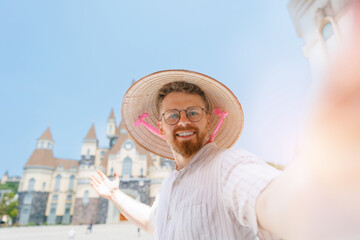 Fototapeta premium Caucasian young male tourist with Viet hat taking selfie in front of amusement park in Nha Trang, travel trip in Vietnam