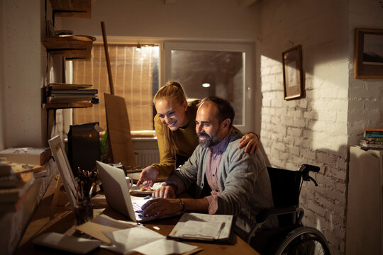 Smiling couple collaborating on laptop in cozy home office at night