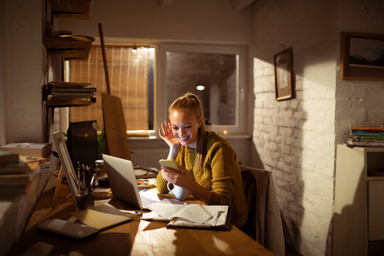 Smiling woman video calling from cozy home office at night