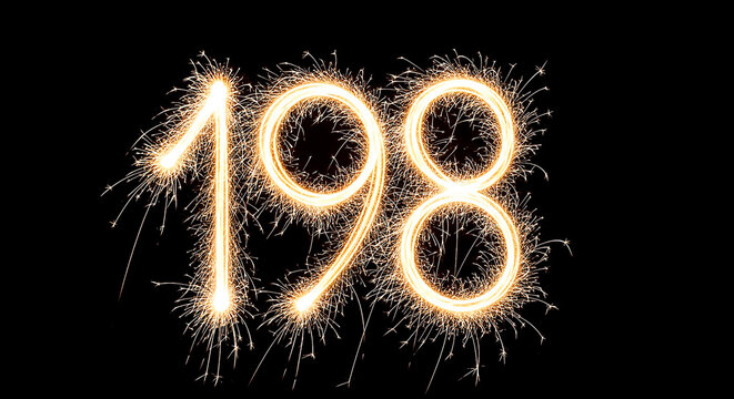 Close-up of glowing sparklers creating the year 1998 with bright golden trails against a dark background, evoking celebration and festivity.