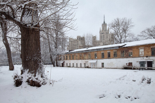 View of a snow-covered courtyard with a historic low-rise building and a Stalinist skyscraper under an overcast winter sky Moscow, Moscow, Russia.